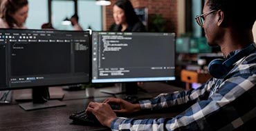 Mann mit Desktop und Keyboard schreibt Code